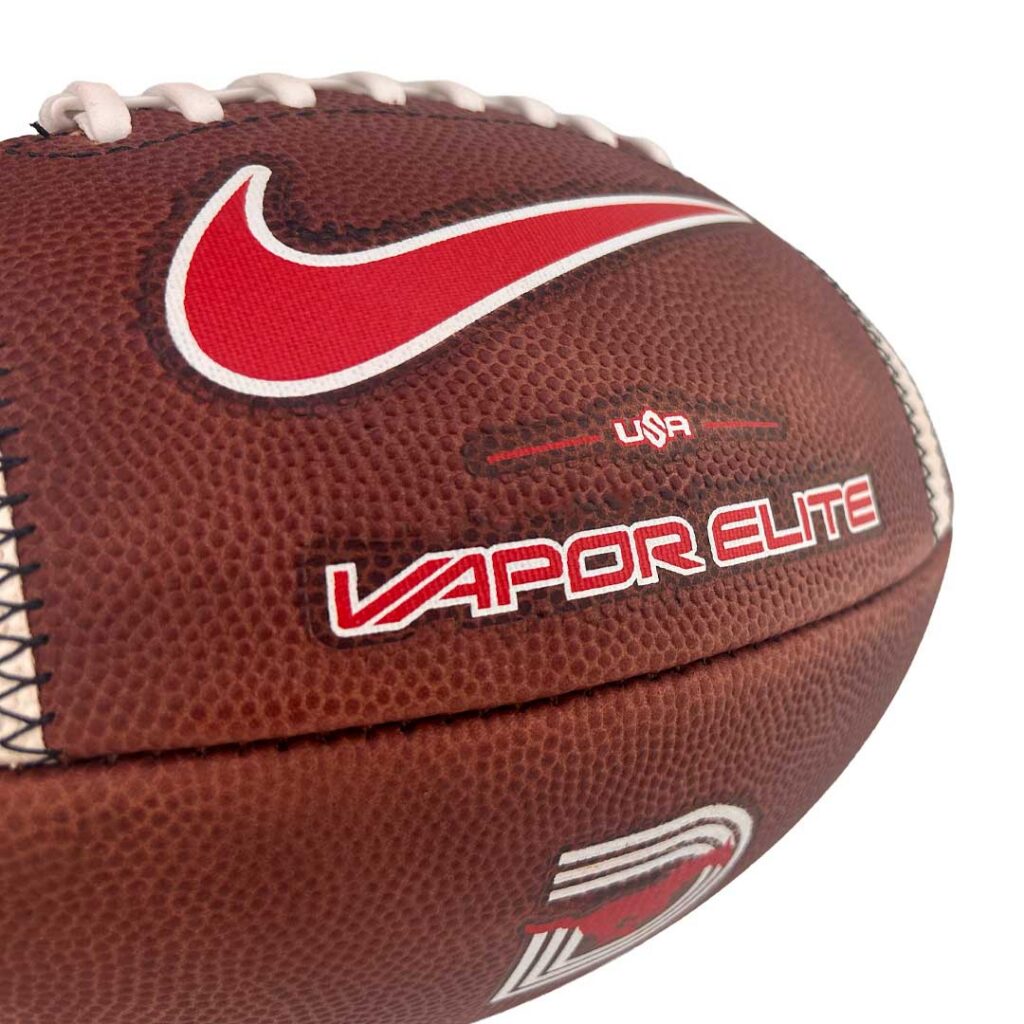Close-up of a brown leather football featuring a red Nike swoosh and the 'VAPOR ELITE' branding.