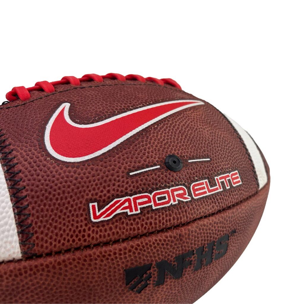 Close-up of a brown leather football with red laces, white-edged red Nike swoosh, and 'VAPOR ELITE' branding visible.