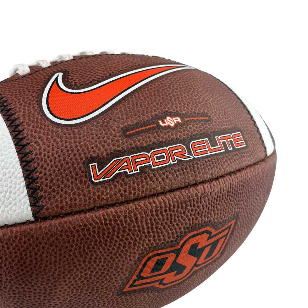 Close-up of a brown leather football showing the orange Nike swoosh and Vapor Elite branding.