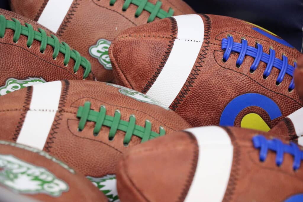 Footballs with green laces and footballs with blue laces piled together.