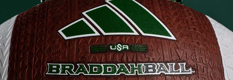 Close-up of a red, textured ball with green and white logo shapes and the text 'BRADDAH BALL' and 'USA'.