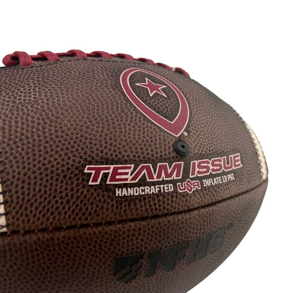 Close-up of a brown leather football with red laces and team issue branding, showing texture and logo details.
