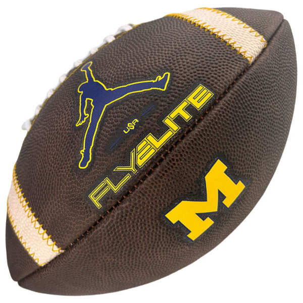 Brown football with tan laces and yellow stitching, featuring a blue jumping-kick silhouette, 'USA' text, 'FLYELITE' in yellow, and a large yellow 'M' logo on the side.