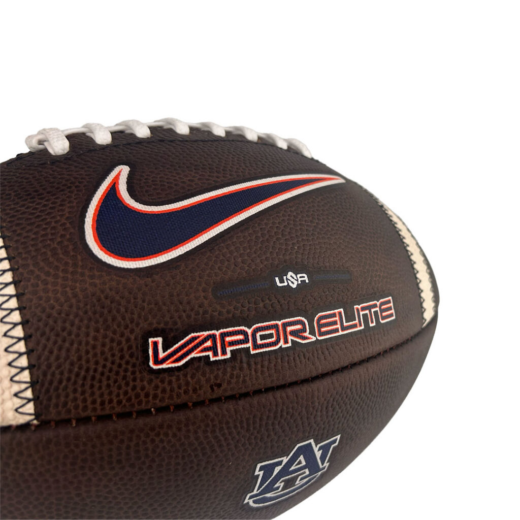 Close-up of a brown leather football showing white laces, a blue-red Nike swoosh patch, and 'VAPOR ELITE' branding with 'USA' text below.