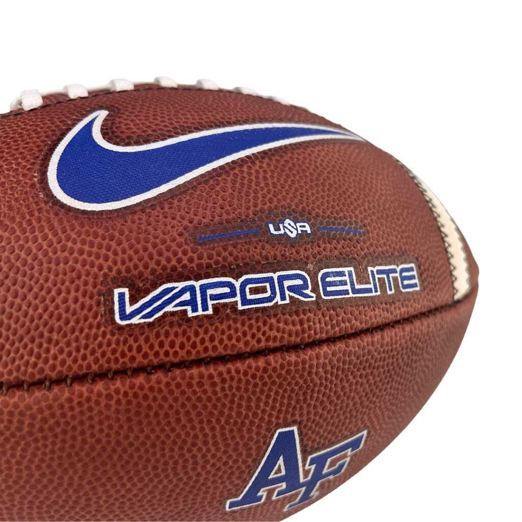Close-up of a brown football featuring a blue Nike swoosh and the words 'Vapor Elite' with 'USA' and 'AC' markings visible