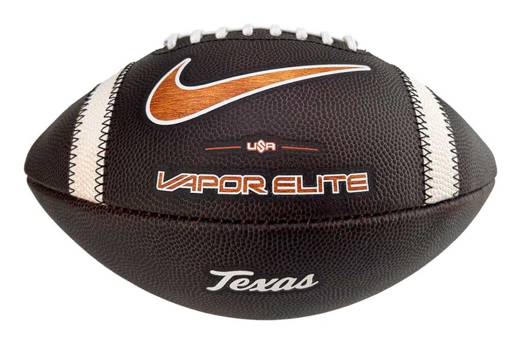 Leather football with white laces and orange Nike swoosh, 'Vapor Elite' branding and 'Texas' text on a brown pebble-grain surface.