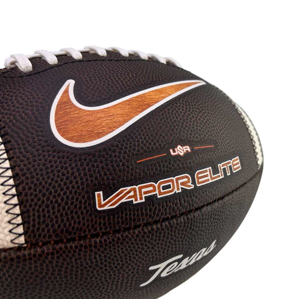 Close-up of a brown leather football with white laces, an orange swoosh logo, and 'VAPOR ELITE' branding on the side.