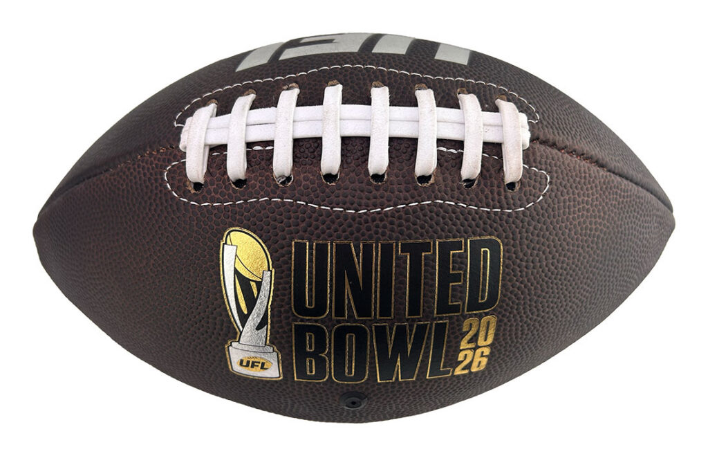 A brown football with white laces and gold-embossed text reading 'UNITED BOWL 2026' beside a small trophy logo marked 'UFL'.