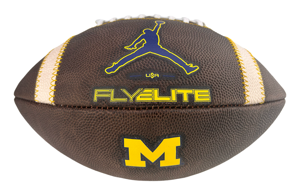 Brown football with yellow Michigan 'M' logo on the lower panel and a blue Jumpman silhouette; 'FLYELITE' text visible on the surface.