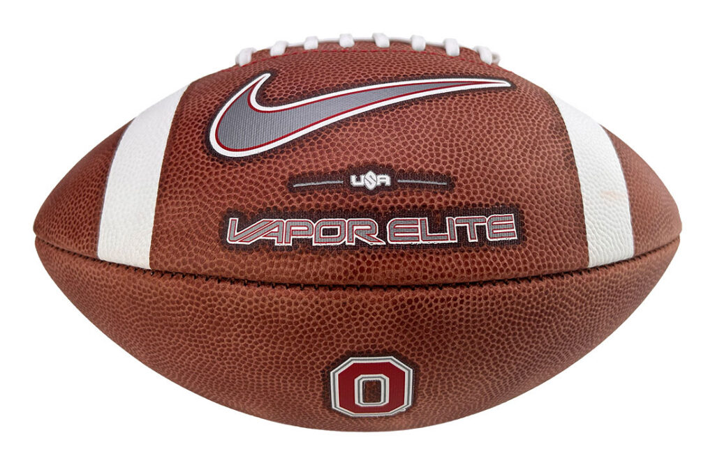 Brown leather football with white laces and two white stripes, Nike swoosh, Vapor Elite branding, and a red Ohio State patch.