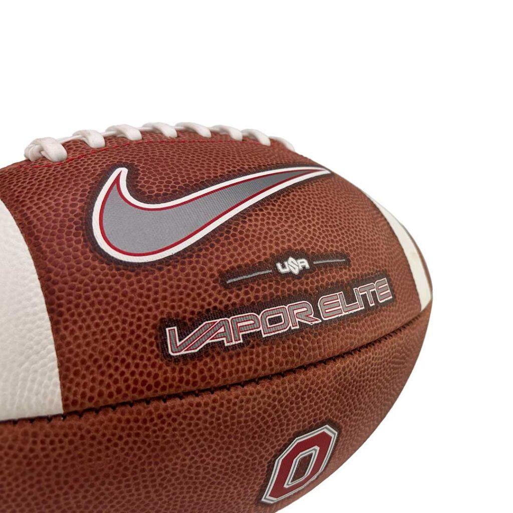 Close-up of a brown leather football with white laces and Nike swoosh; Vapor Elite branding visible.