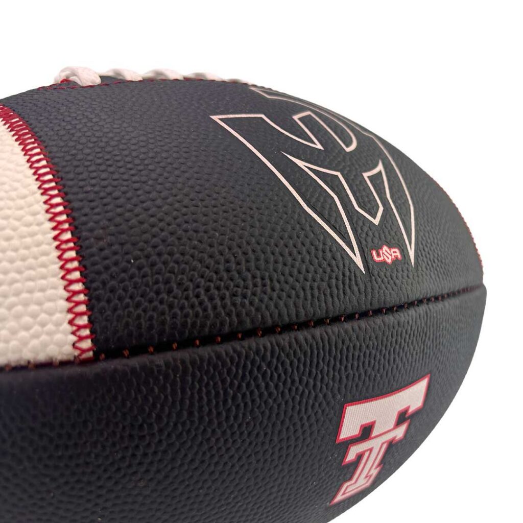 Close-up of a textured football with red stitching, dark panels, and a small USA emblem on the side.